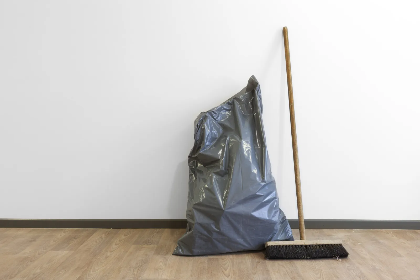 Müllsack und Besen an der Wand einer besenrein übergebenen Wohnung