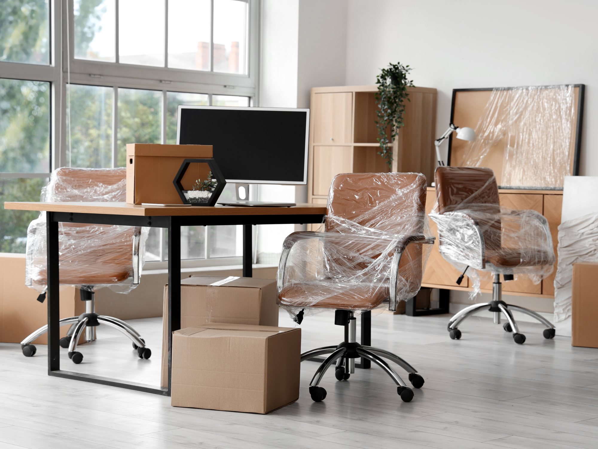 Büro mit in Folie verpackten Stühlen, Schreibtisch und Umzugskartons vor der Räumung