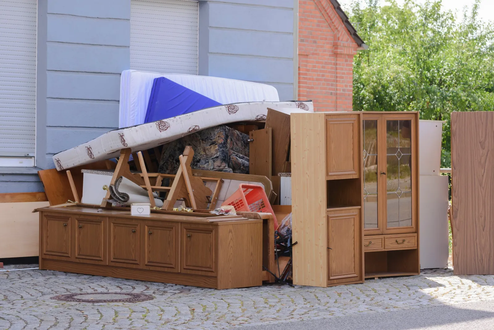 Sperrmüllhaufen mit Schrankwand, Matratzen und Kommode vor einem Haus