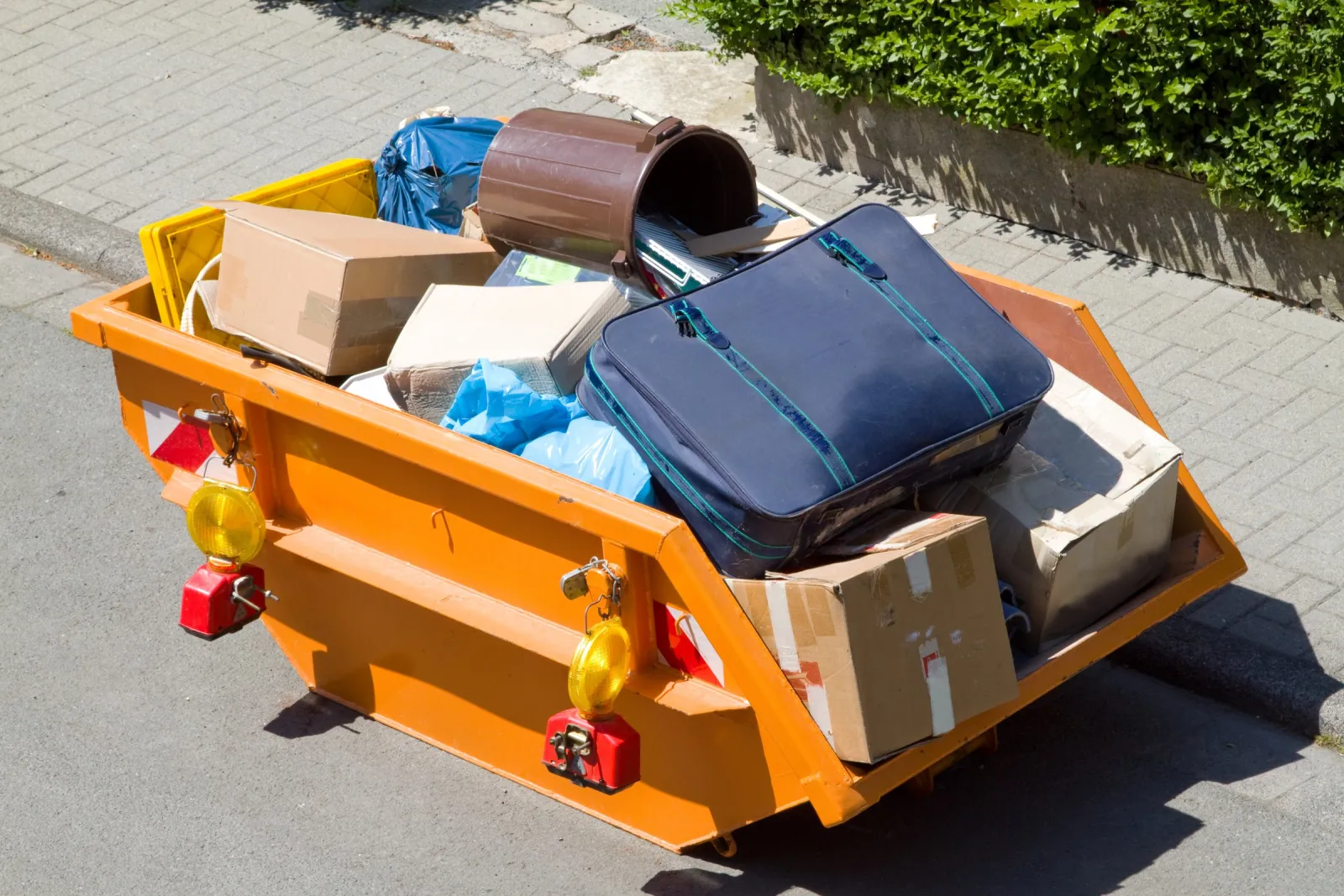 Absetzmulde mit Kartons, Koffer und Tonne am Straßenrand