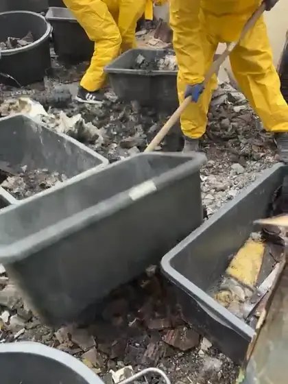 Video: Mitarbeiter in Schutzanzügen räumen Brandschutt in Wannen